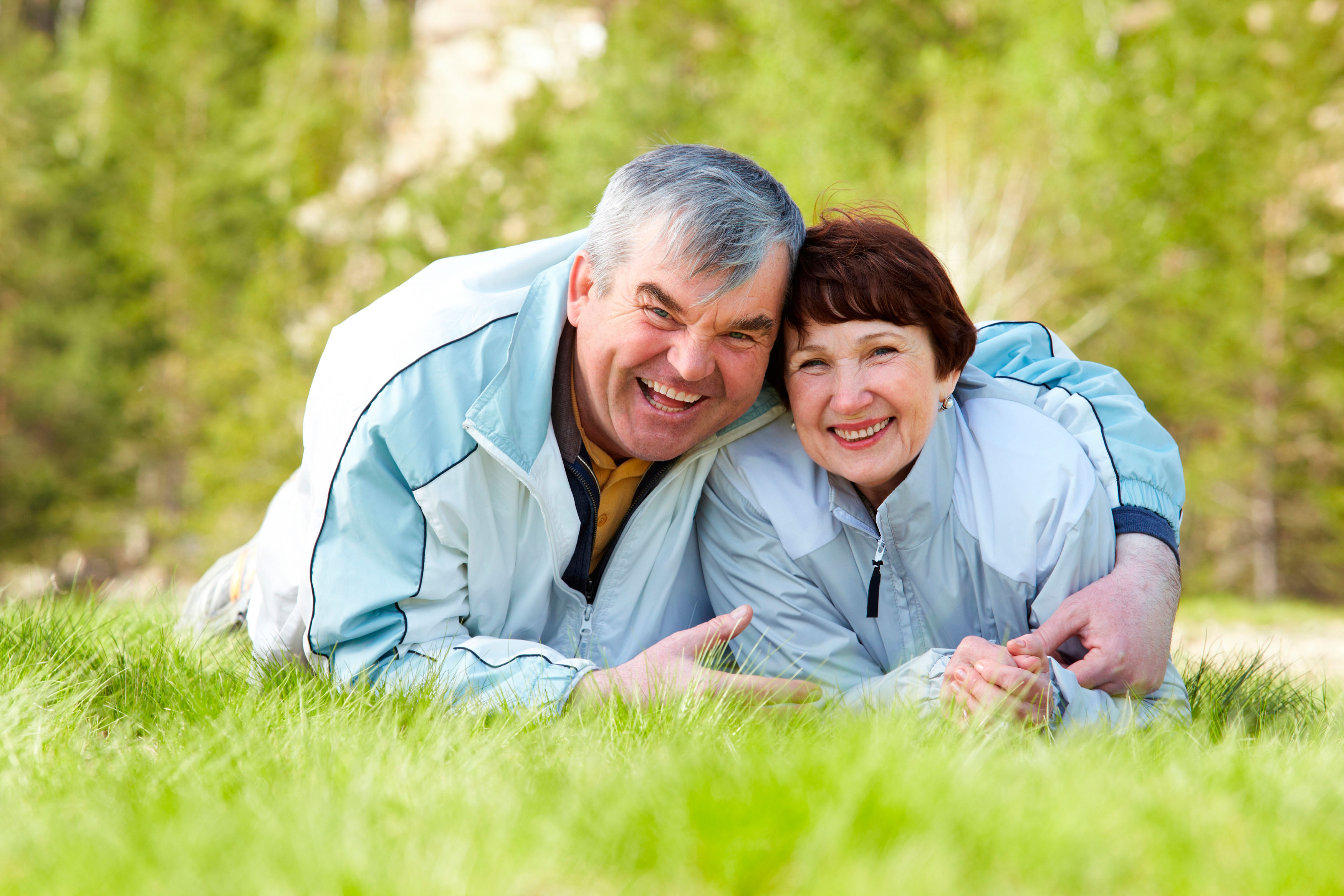 Older man hugs his wife while lying on a grass